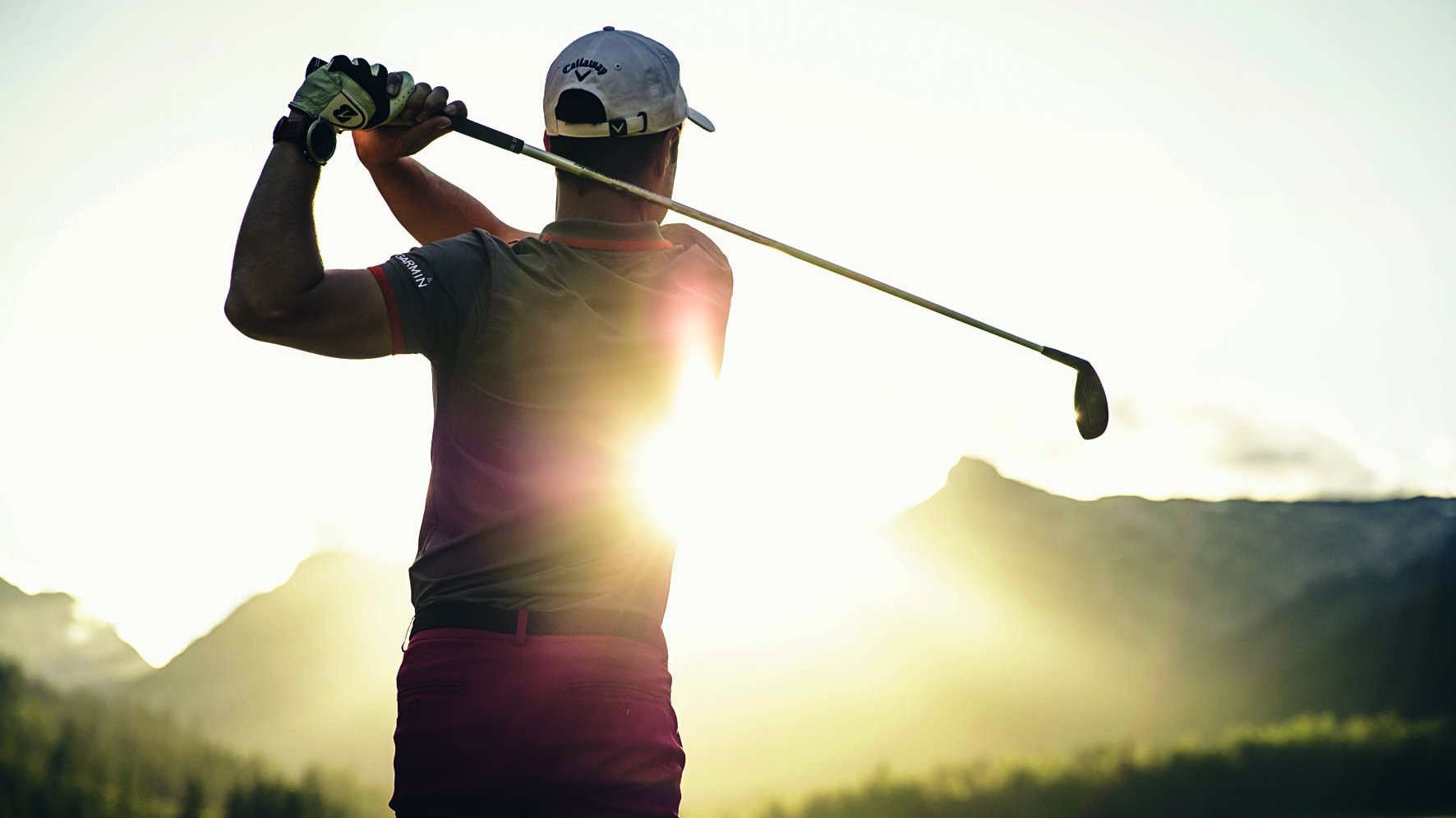 Golfschwung im Sonnenuntergang Golfer schwingt Schläger bei Sonnenuntergang vor beeindruckender Bergkulisse