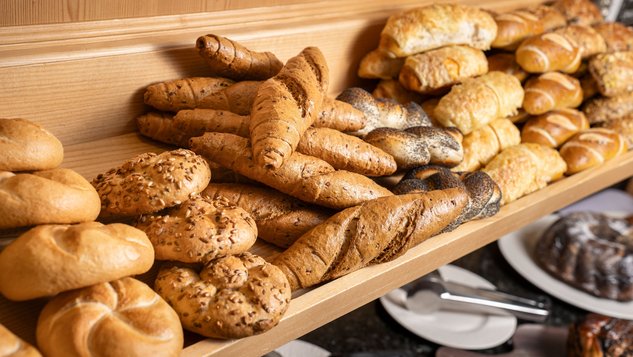 Vielfalt an frisch gebackenem Brot auf einem Holzregal, darunter Brötchen und Baguettes.