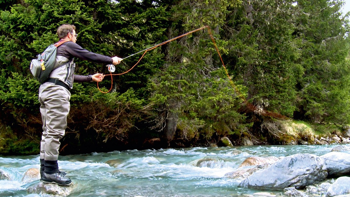 Person fly fishing on a clear mountain river, surrounded by trees.