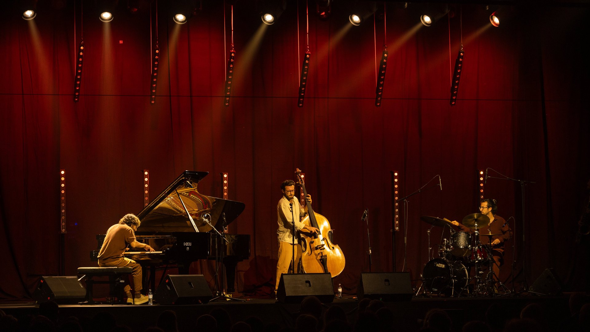 Jazz trio plays on a stage with a red curtain and atmospheric lighting.
