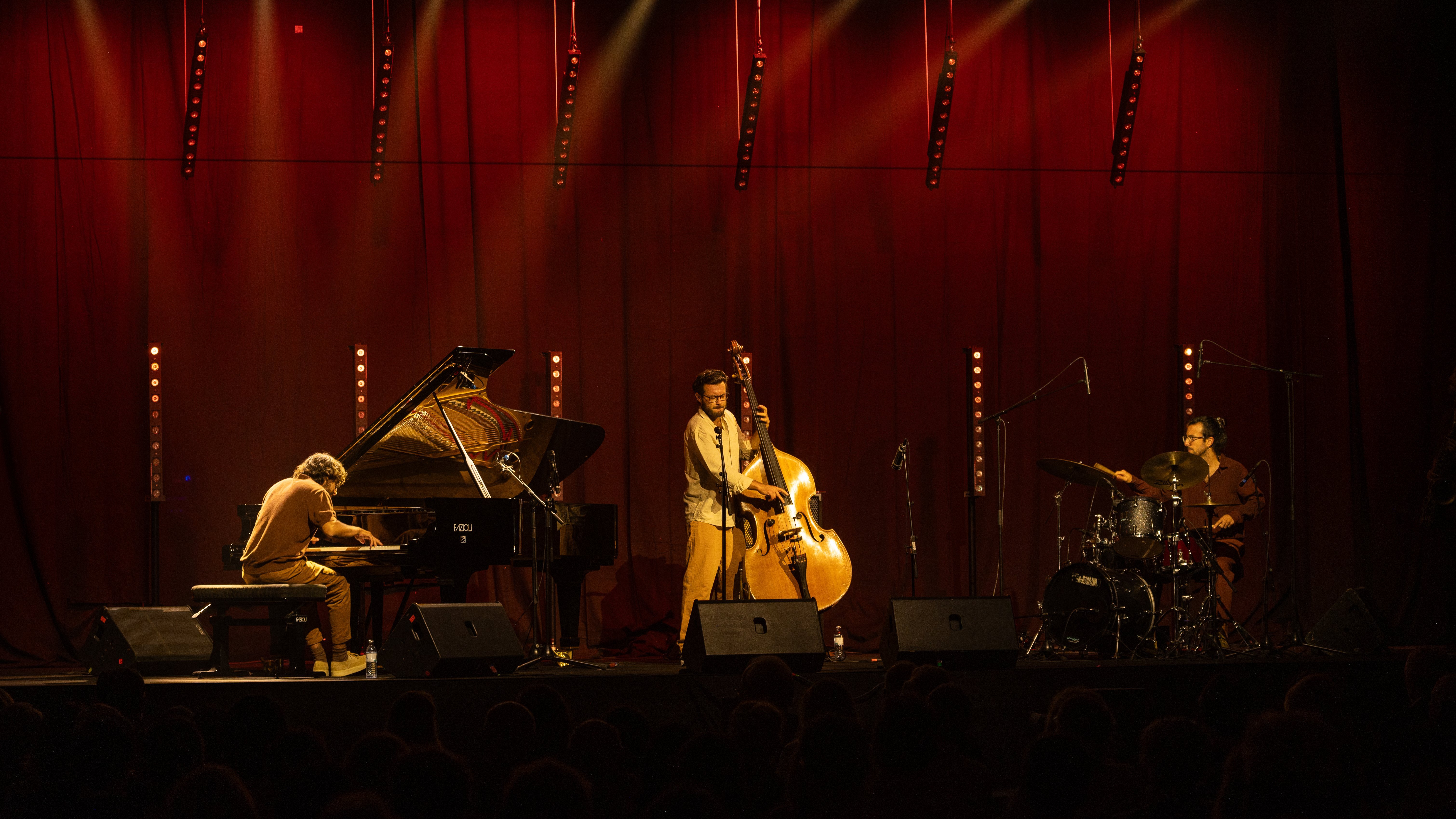 Jazztrio spielt auf Bühne mit rotem Vorhang und stimmungsvoller Beleuchtung.
