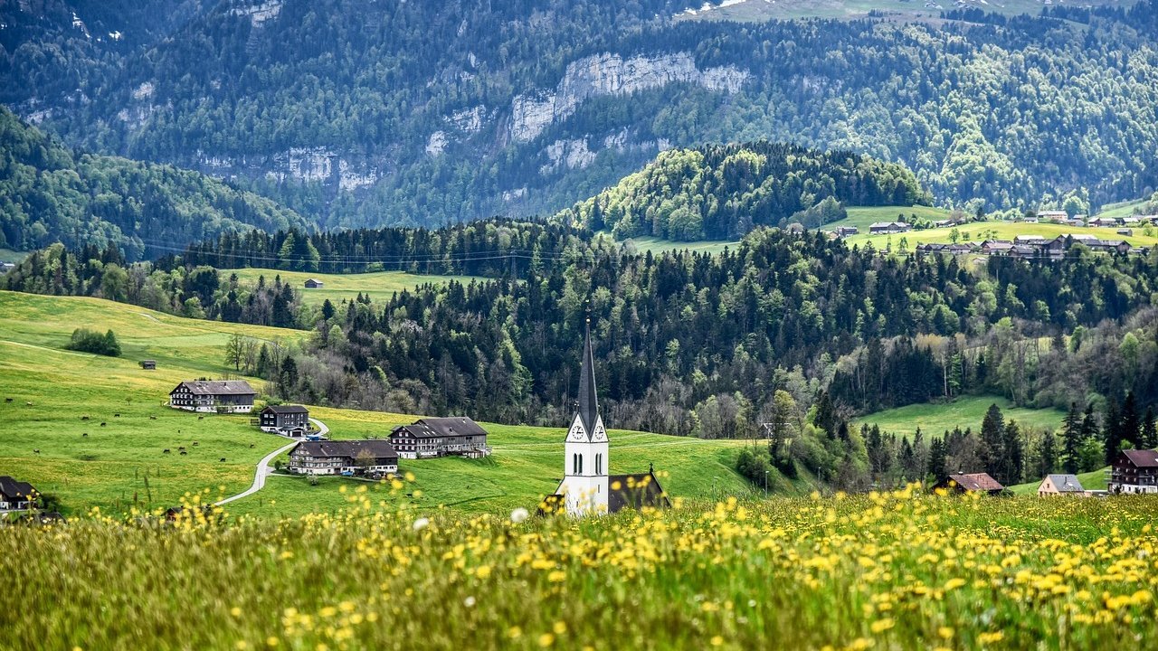 Grüne Wiesen und Kirche vor beeindruckendem Bergpanorama im Bregenzerwald.