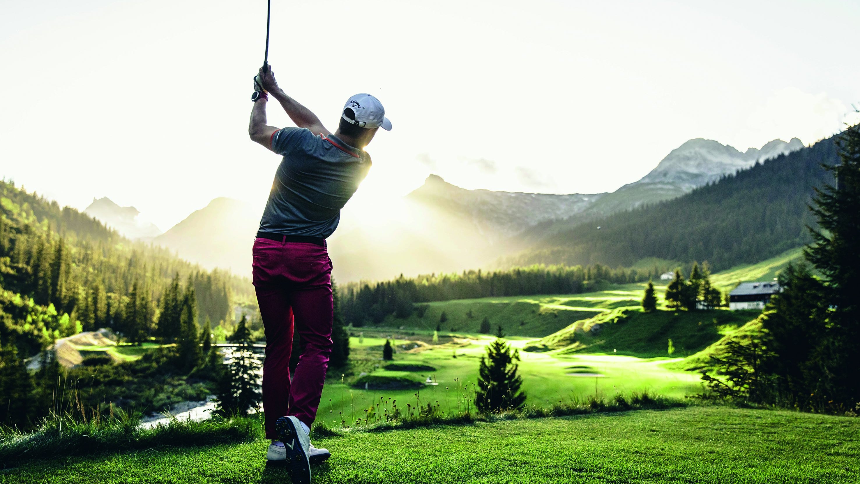 Golfvergnügen im Sonnenuntergang Golfer schwingt den Schläger bei Sonnenuntergang in einer beeindruckenden Berglandschaft.