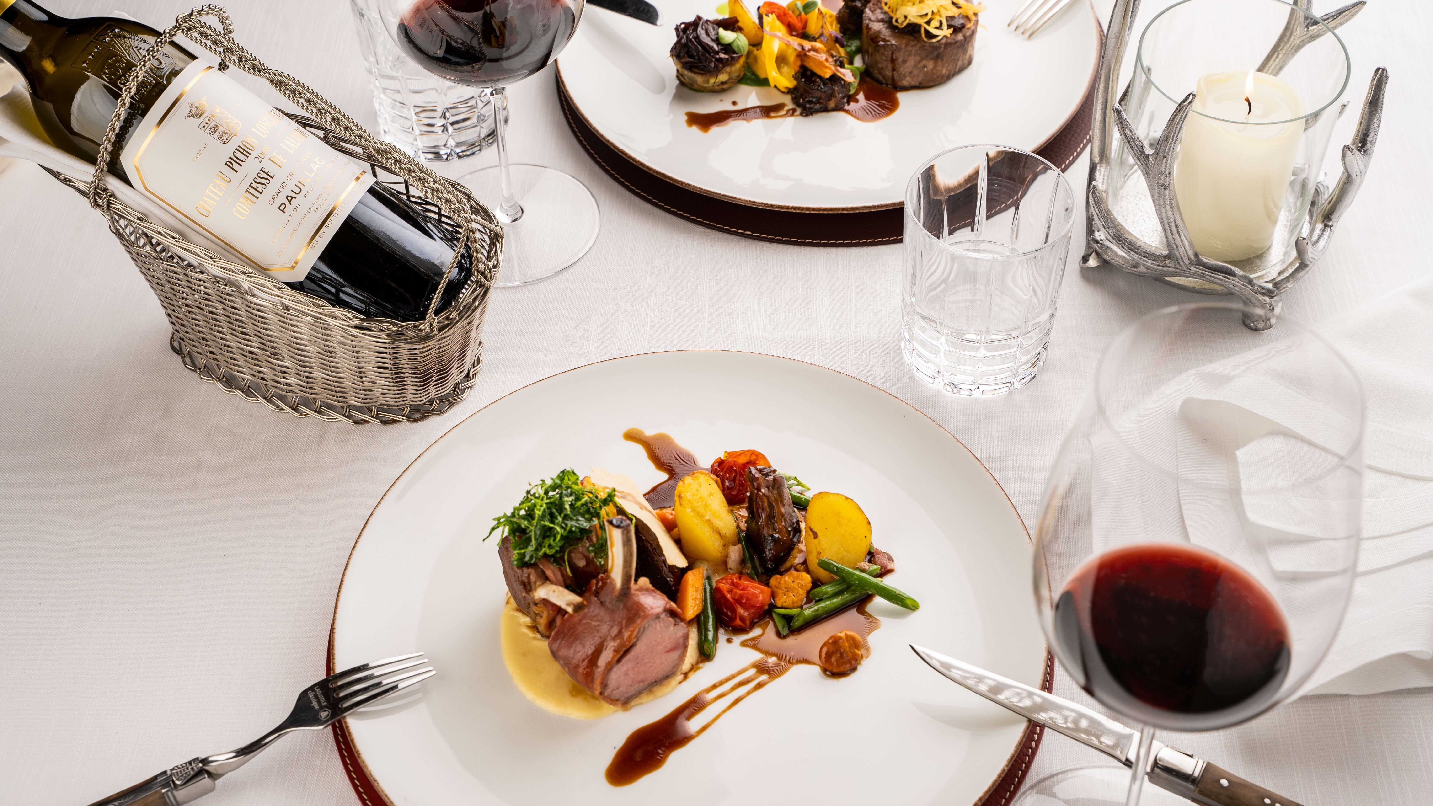 Elegantes Dinner-Setting Zwei kunstvoll angerichtete Teller mit Rotwein und Kerze auf weißer Tischdecke.