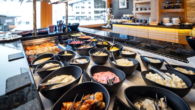 Buffet mit verschiedenen Frühstücksoptionen in schwarzen Schalen, darunter Früchte und Joghurt.