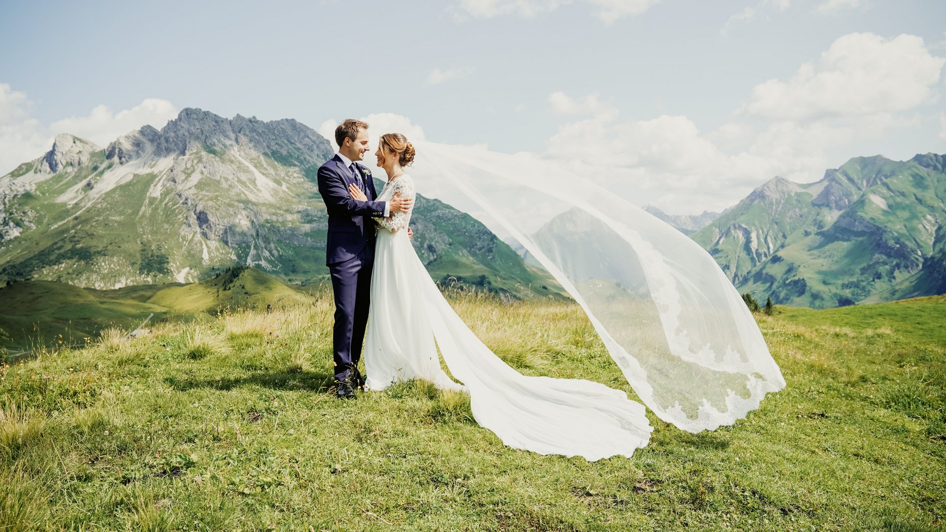 Hochzeitspaar in eleganter Kleidung vor beeindruckender Bergkulisse unter klarem Himmel
