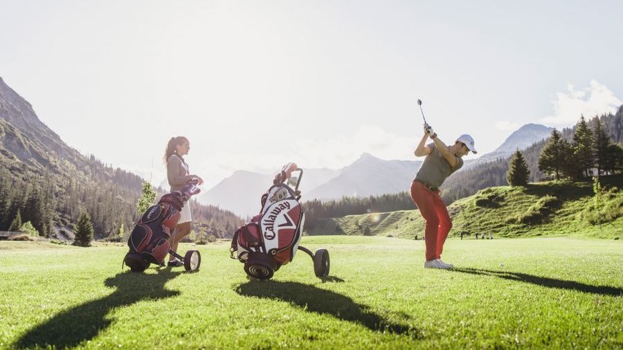 Golfen in den Alpen Zwei Frauen spielen Golf auf einem sonnigen Platz in den Bergen.