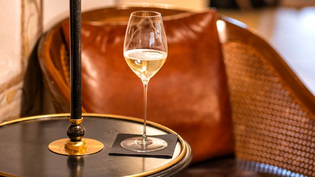 Gemütliche Lounge mit einem Weinglas auf einem Tisch und einer stilvollen Lampe im Hintergrund.