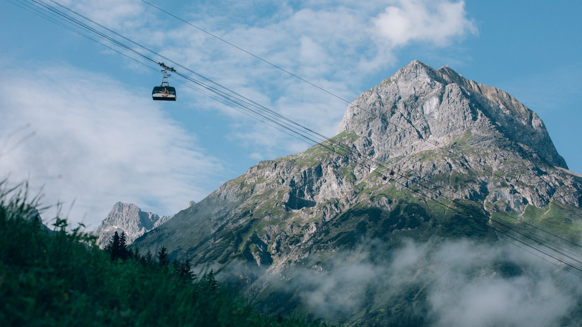 Cable car travels across green meadows with a majestic mountain in the background.