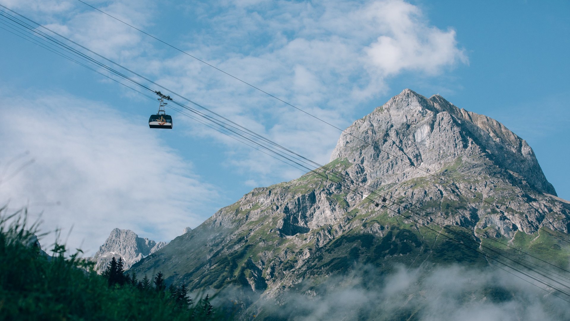 Cable car travels across green meadows with a majestic mountain in the background.