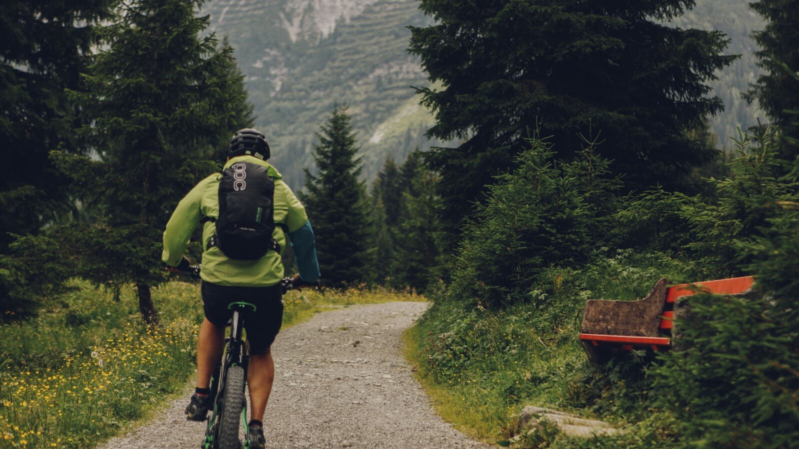 Person fährt mit einem Mountainbike auf einem Schotterweg durch einen Wald.