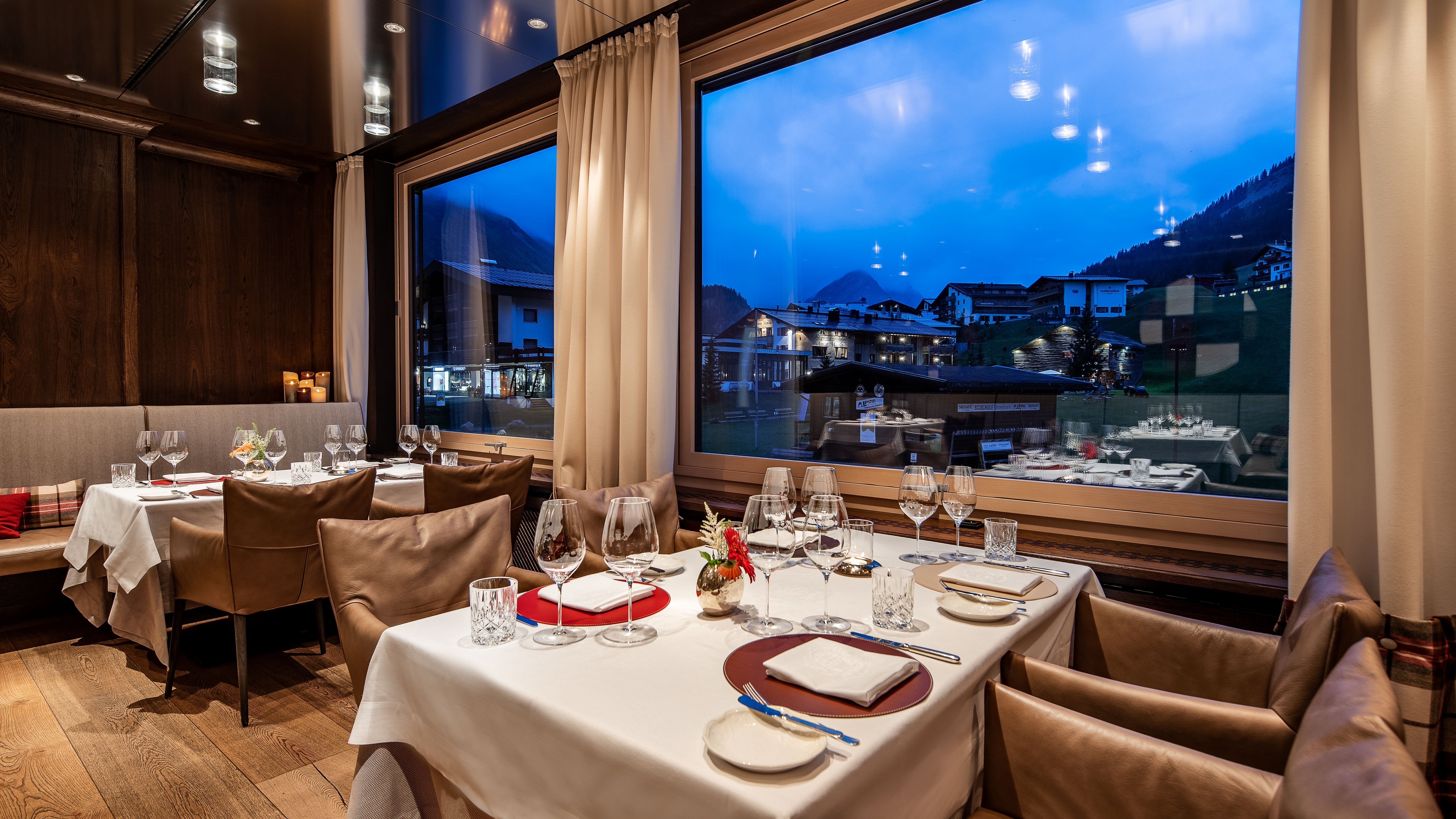 Elegante Abendstimmung Stilvoll gedeckte Tische vor einer großen Fensterfront mit Bergblick in der Dämmerung.