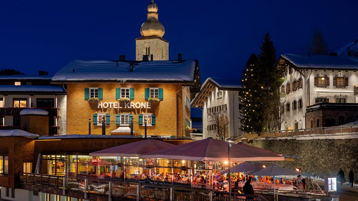Romantik Hotel “Die Krone von Lech” at night, festively illuminated, with snow-covered roofs and trees decorated with lights.