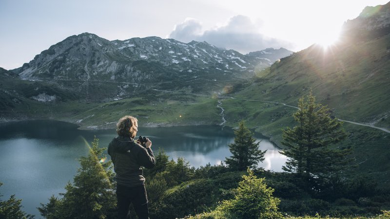 Person blickt auf einen Bergsee mit umliegender Berglandschaft.