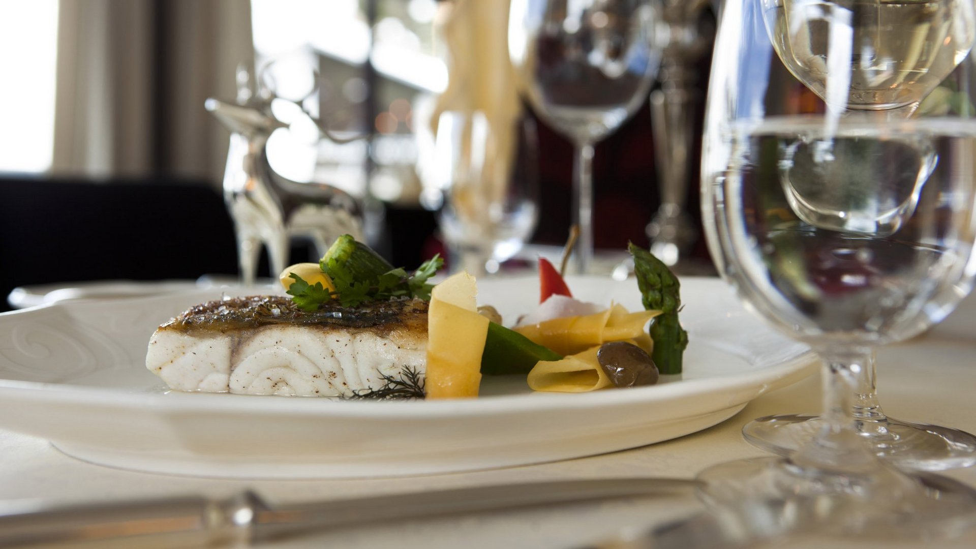 Elegant dish with fish fillet and vegetables on an elegantly laid table.